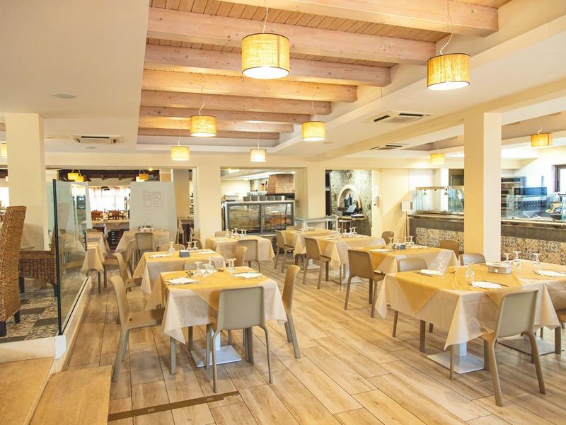Salle de restaurant lumineuse avec tables en bois et chaises grises.