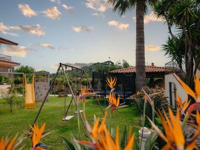 Jardin avec une balançoire et des fleurs d'oiseau de paradis devant une maison de vacances sous un ciel bleu.