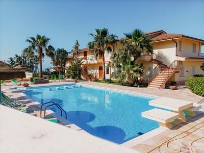 Un hôtel avec une grande piscine extérieure, entourée de palmiers et de chaises longues sous un ciel bleu.