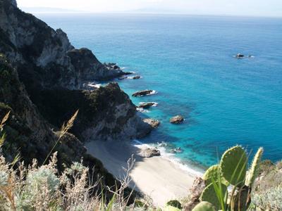 Plage avec eau bleue claire et côte rocheuse, entourée de végétation verte.