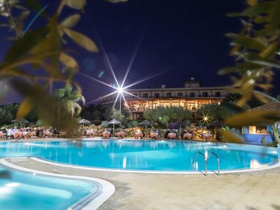 Piscine d'hôtel éclairée avec chaises longues et arbres la nuit.