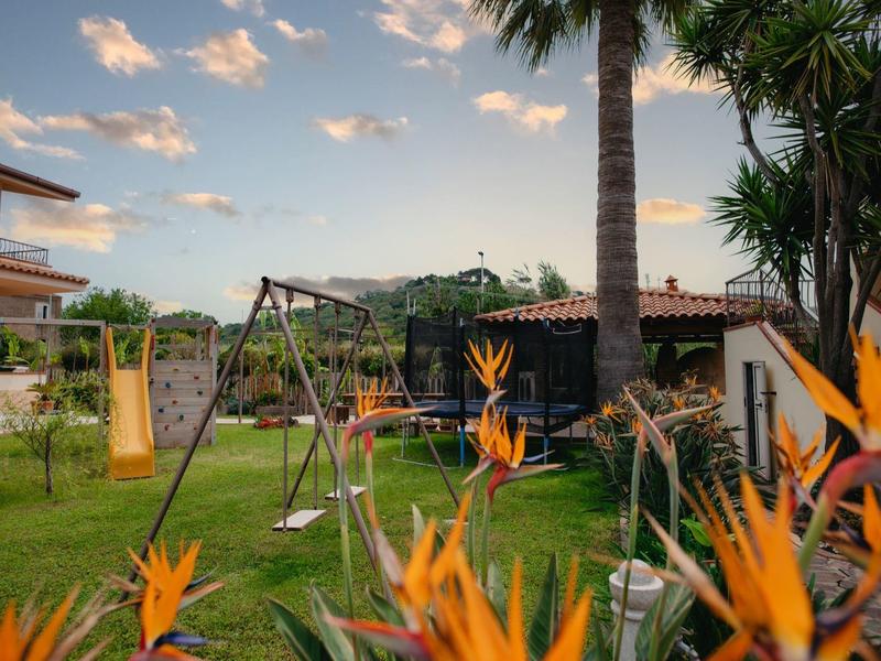 Jardin avec une balançoire et des fleurs d'oiseau de paradis devant une maison de vacances sous un ciel bleu.