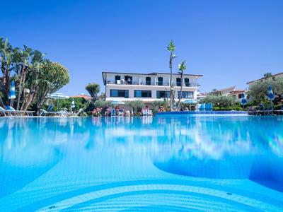 Duży niebieski basen przed wielopiętrowym hotelem pod bezchmurnym niebem.