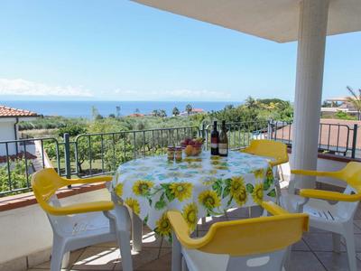 Balkon z stołem i krzesłami, widok na morze i słoneczne niebo w tle.