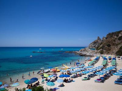 Plaża z leżakami i parasolami przy czystym niebieskim morzu i skalistym wzgórzu