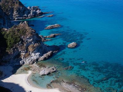 Przejrzysta turkusowa woda otacza skaliste wybrzeże z małą piaszczystą plażą.