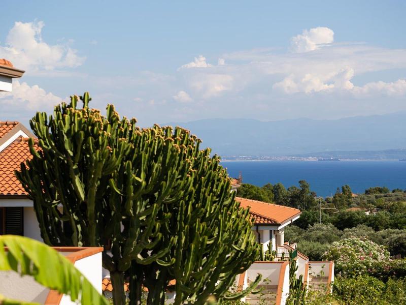 Widok na hotel wakacyjny z kaktusami i morzem w tle pod błękitnym niebem.
