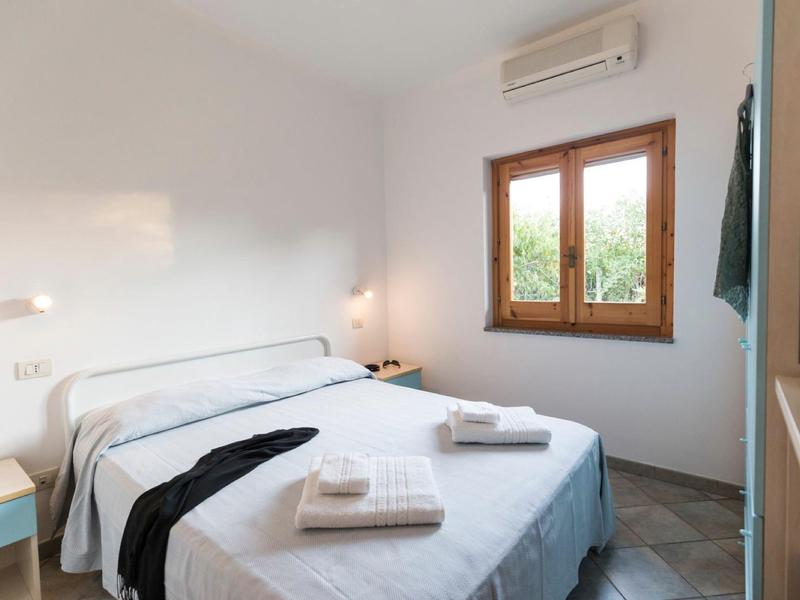 Jasna sypialnia z łóżkiem podwójnym i oknem z widokiem na zieleń.