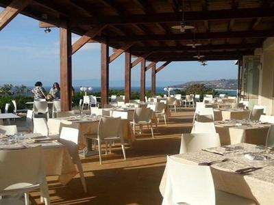 Terrasse extérieure couverte avec des tables blanches dressées et vue sur la mer en arrière-plan.