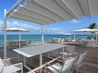 Espace extérieur moderne avec tables et chaises sur terrasse en bois face à la mer.