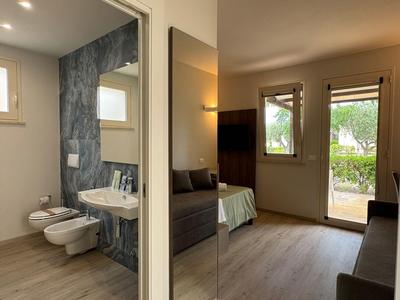 Modern hotel room with bathroom, seating area, and garden access in daylight.