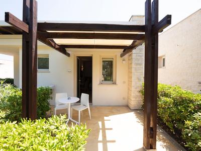 Small paved patio with wooden beams, two white chairs, and abundant greenery at the hotel.