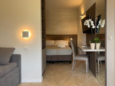Compact hotel room with bed, desk, chair, sofa, and decorative lighting.