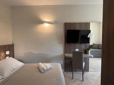 Modern hotel room with double bed, TV, and desk in neutral colors.