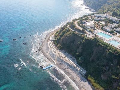 Aerial view of a coastal hotel resort with swimming pools and a pebble beach.