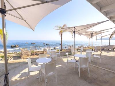 Terrace with white tables and chairs, overlooking the sea and rocks under a clear sky.