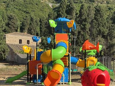 Colorful playground with slides and climbing structures in front of a wooded hill.