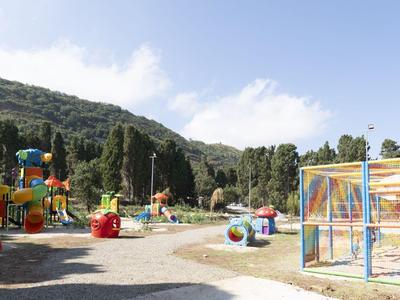 Children's playground with colorful equipment against a forested hill in a sunny hotel setting.