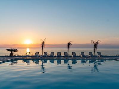 Pool with lounge chairs and coconut palms at sunset by the sea.