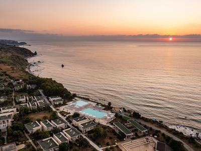 Aerial view of a hotel with a pool on a calm beach at sunset.