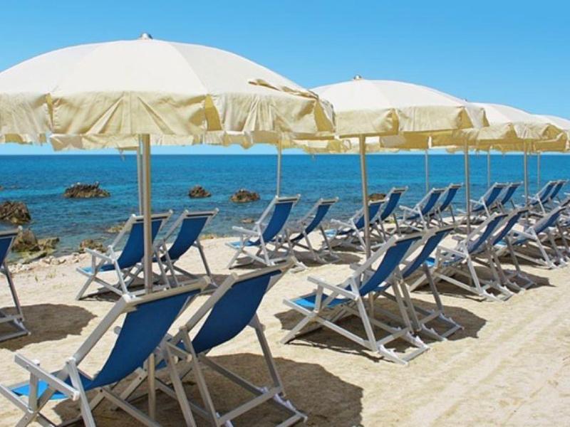 Rangée de chaises longues bleues avec parasols blancs sur plage de sable près de la mer bleue.