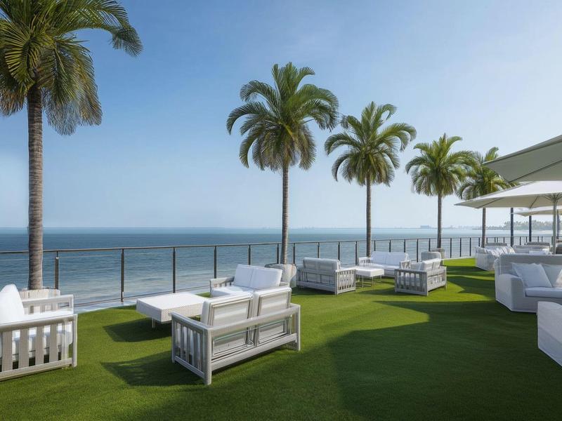 Terrasse sur le toit avec pelouse verte, sièges blancs et vue sur l'océan sous un ciel bleu.