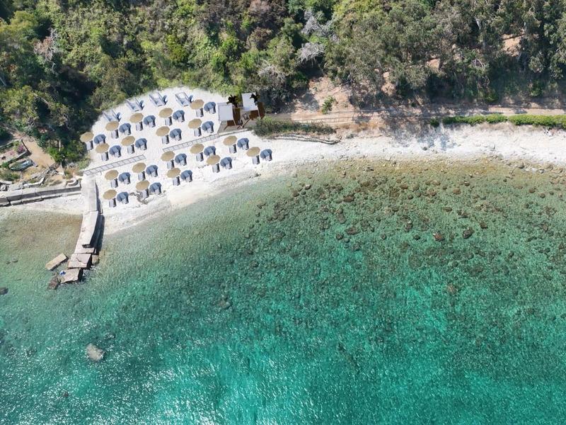 Vue aérienne d'une plage calme avec des transats et une eau turquoise claire.