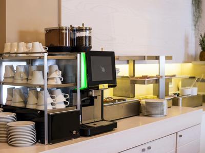Moderne koffiemachine met kopjes en borden in een lichte buffetruimte.
