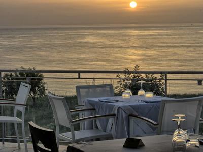 Terrazza con tavoli apparecchiati e sedie con vista sul sole sopra il mare calmo.