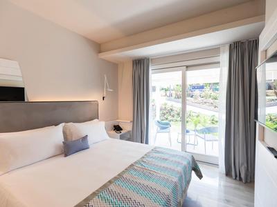 Lichte hotelkamer met tweepersoonsbed, balkon en uitzicht op een rustige waterweg.