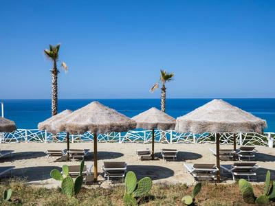 Strandliegen mit Sonnenschirmen, Palmen und Blick auf das blaue Meer unter klarem Himmel