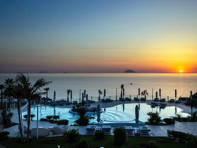 Hotelzwembad met ligstoelen en palmbomen bij zonsondergang aan zee