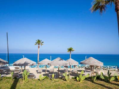 Strandresort met ligstoelen en rieten parasols tegen een heldere blauwe lucht en zee.