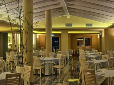 Ruime hotelrestaurant met gedekte tafels en warm geel licht.