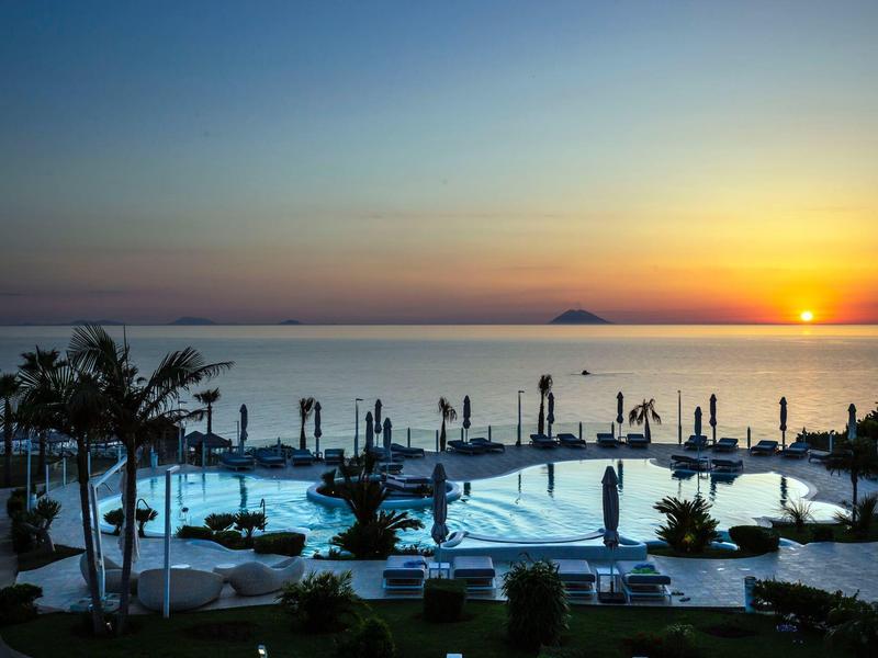 Hotelzwembad met ligstoelen en palmbomen bij zonsondergang aan zee