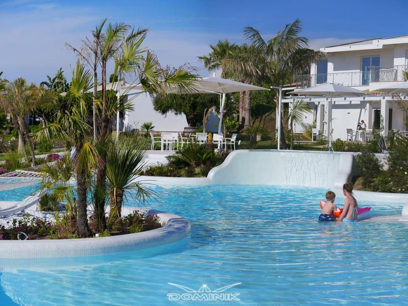 Groot zwembad met tropische planten en een hotelgebouw op de achtergrond op een zonnige dag.