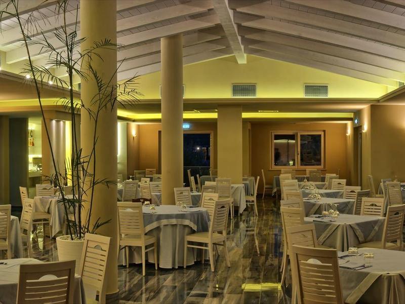 Ruime hotelrestaurant met gedekte tafels en warm geel licht.