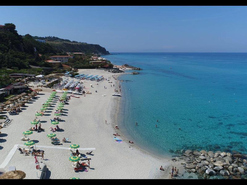 Strand met ligstoelen en parasols naast helder turquoise water en rotsen
