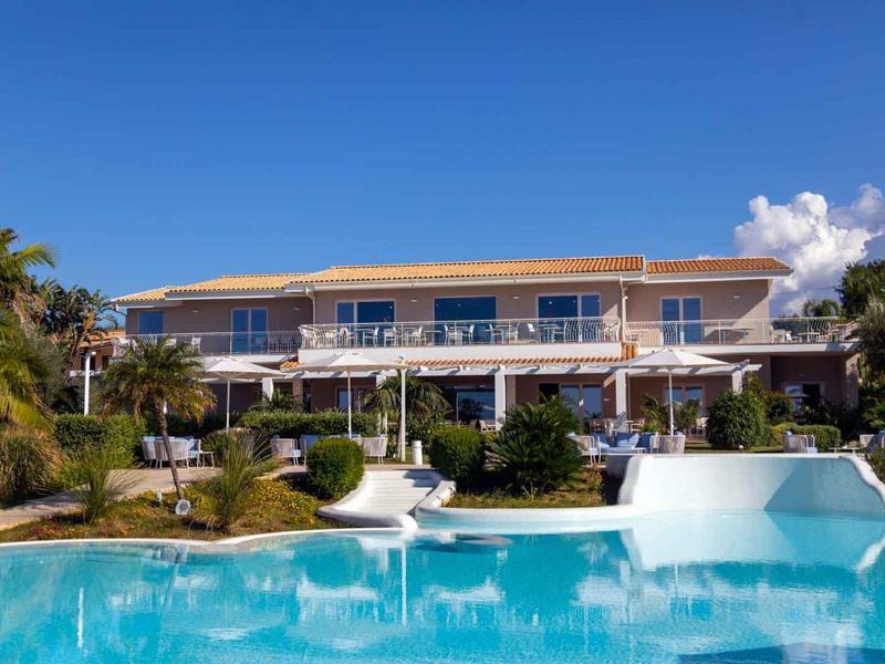 Luxe villa met groot zwembad en weelderige tuin onder een heldere blauwe lucht.