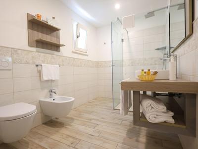 Modern bathroom with toilet, bidet, glass shower, wooden vanity, and towel shelves.