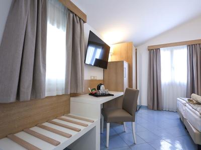 Bright hotel room with two windows, desk, chair, TV, and neatly made twin beds.