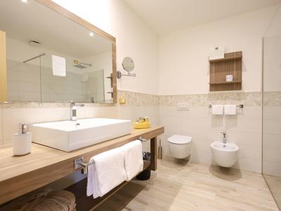 Modern hotel bathroom with wooden counter, rectangular sink, mirror, toilet, and bidet.
