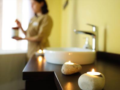 Close-up of lit candles and soap near a white sink in a softly lit bathroom.