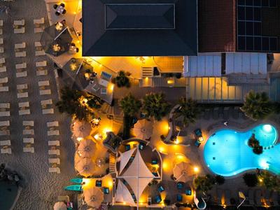 Scatto notturno di una piscina d'hotel illuminata con lettini su una spiaggia sabbiosa.