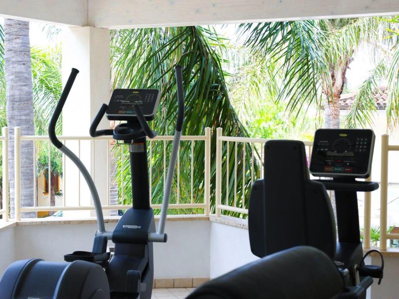 Compact gym room with exercise machines and large windows overlooking tropical greenery.