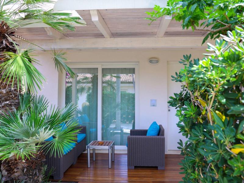 Cozy outdoor patio with armchairs and table, surrounded by lush greenery and tropical plants.