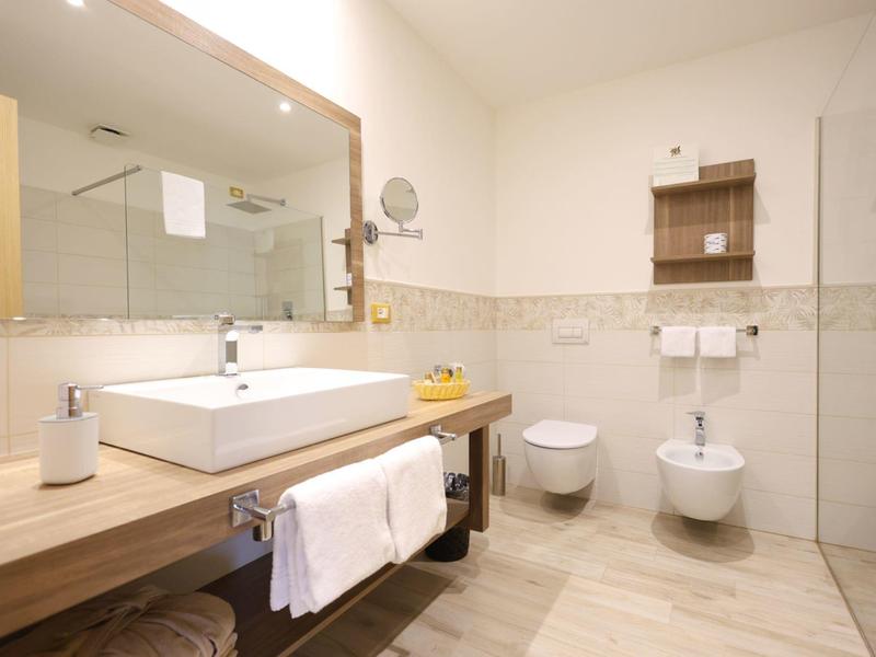 Modern hotel bathroom with wooden counter, rectangular sink, mirror, toilet, and bidet.