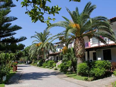 Chemin avec des palmiers et des buissons devant un bâtiment hôtelier sous un ciel ensoleillé.
