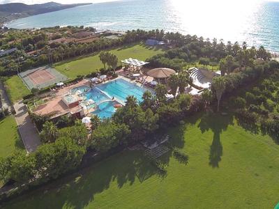 Vue aérienne d'un hôtel avec piscine près de la plage et pelouse verte au premier plan.