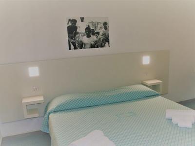 Une chambre d'hôtel simplement meublée avec un lit double, une couette bleue et un éclairage mural.